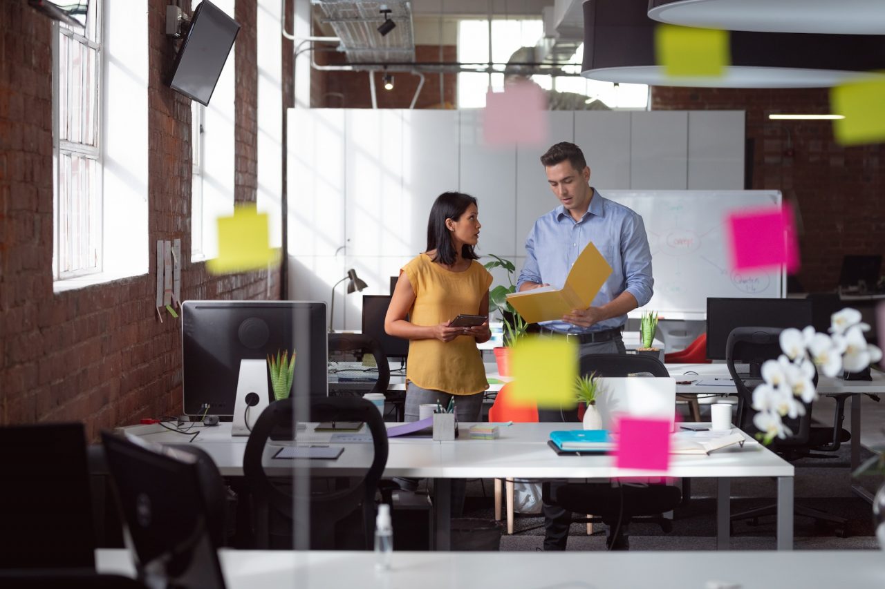 caucasian male and female colleague discuss tablet and file view through glass wall and memo notes
